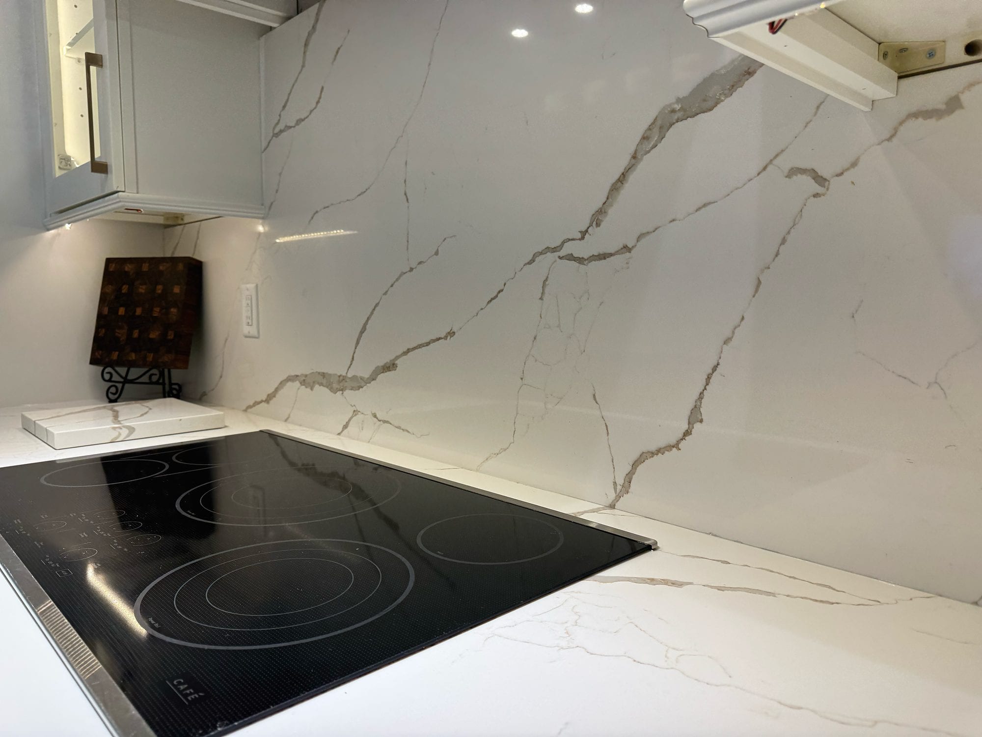 Veined countertop and full-height backsplash beside a black glass cooktop