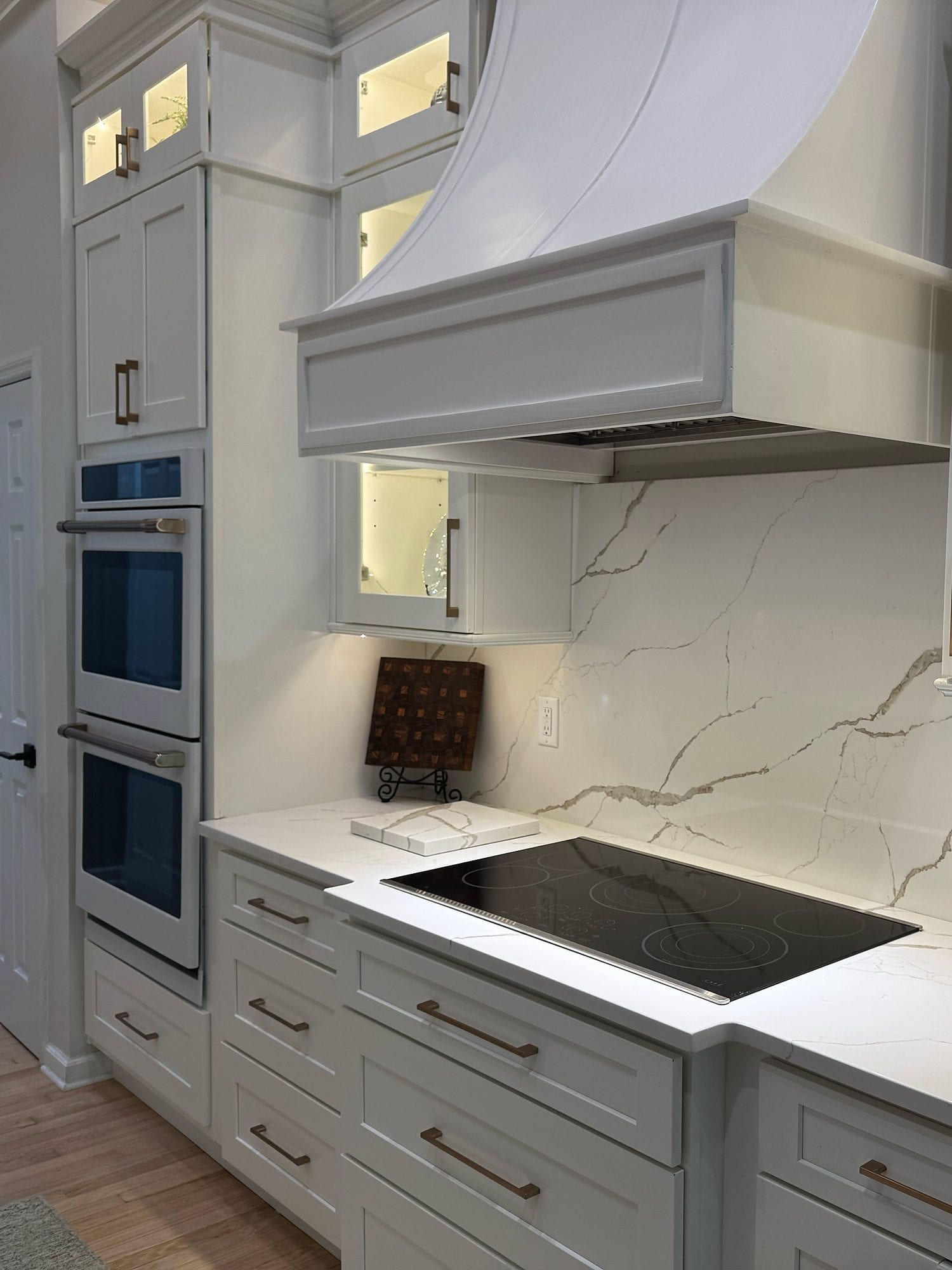 Finished cooking wall with a statement hood, double ovens, white cabinetry, and veined backsplash