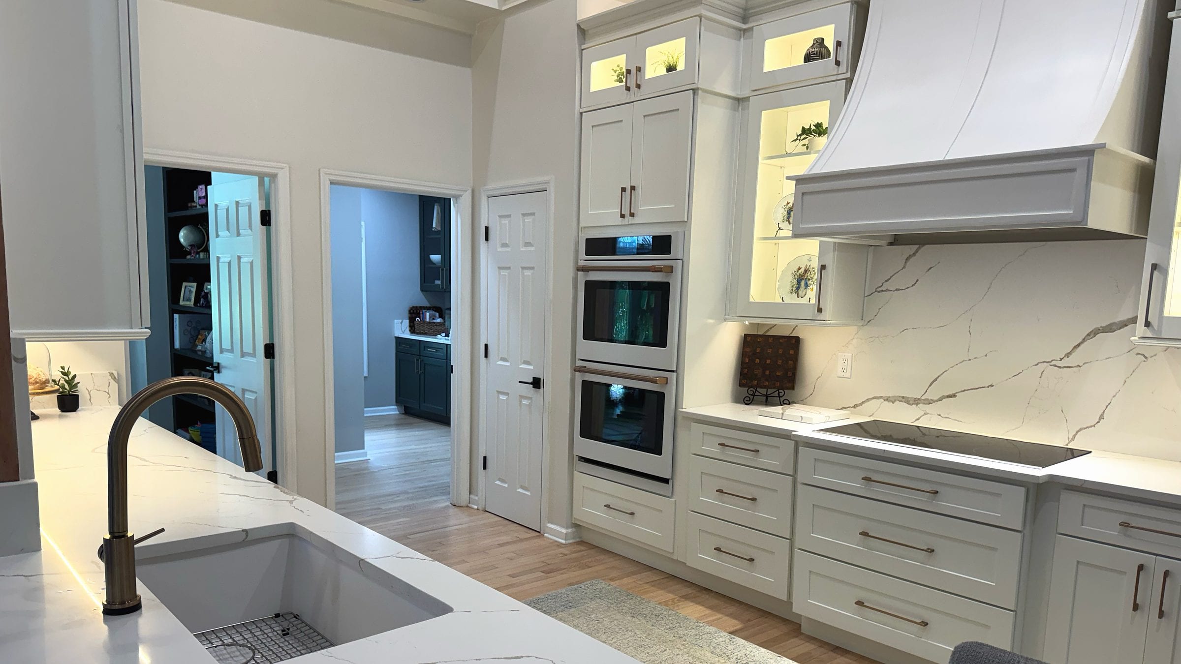 Kitchen island with an undermount sink facing painted cabinetry and a statement range hood