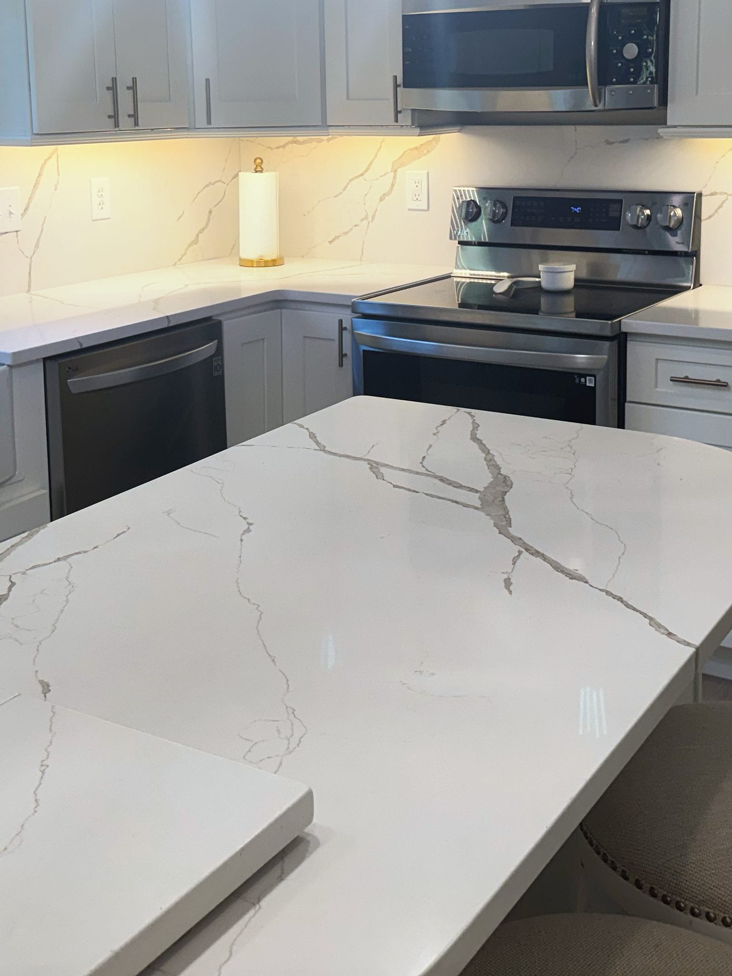 Finished kitchen detail with veined counters, painted cabinetry, dishwasher, range, and island